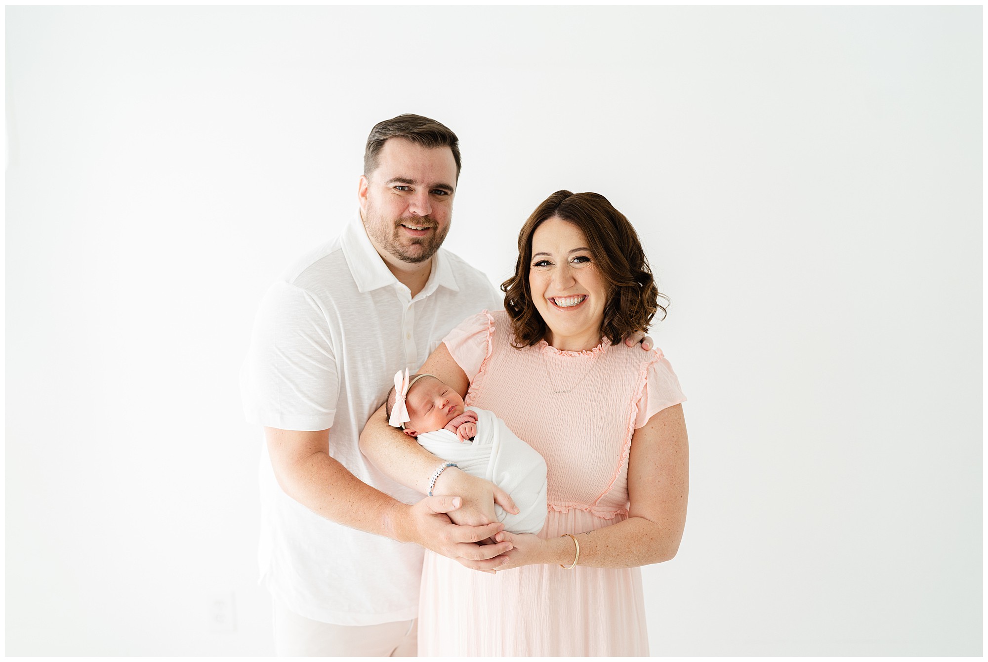 New parents holding a newborn baby and smiling for the camera during a Marietta newborn session.