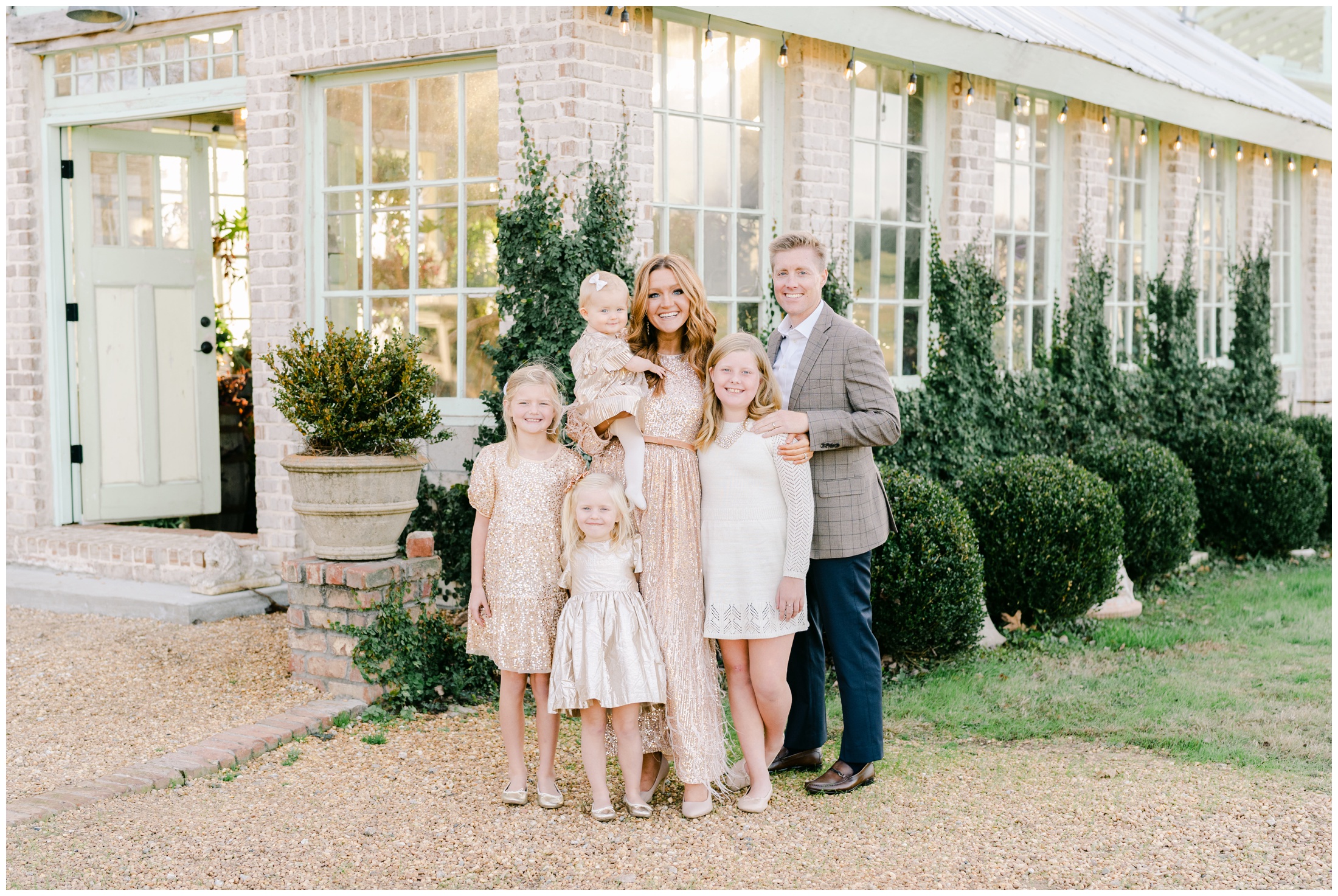 Parents and their four daughters stand in front of the greenhouse at West Milford Farm, smiling for a photo taken by Atlanta photographer Lindsey Powell.