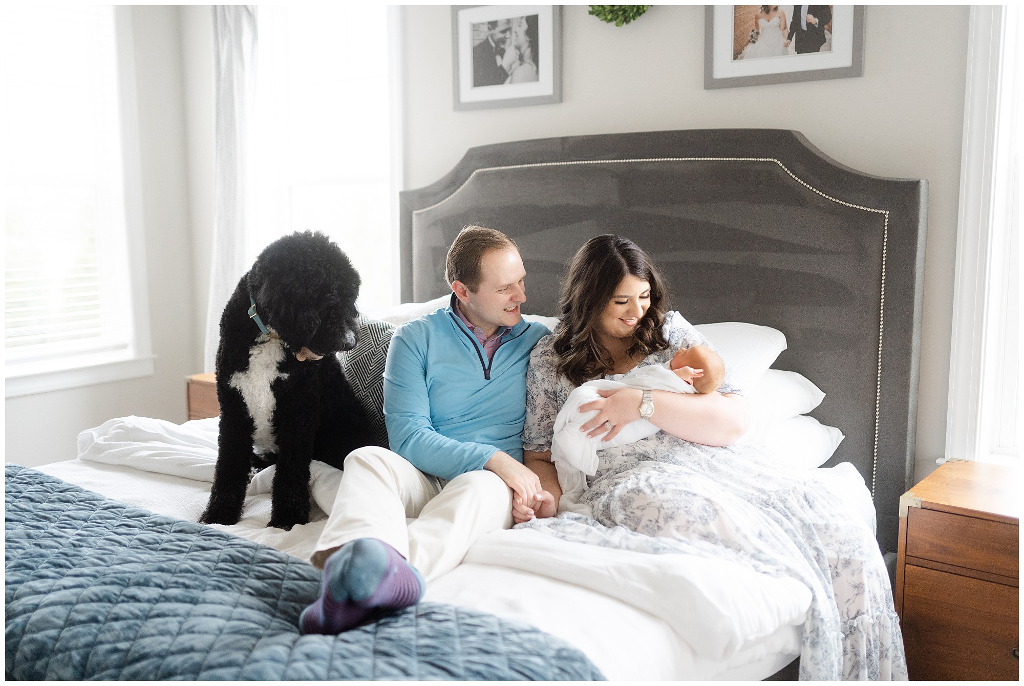 Parents sitting on their bed smiling down at their newborn baby with a black dog during their Atlanta in home newborn photography session.