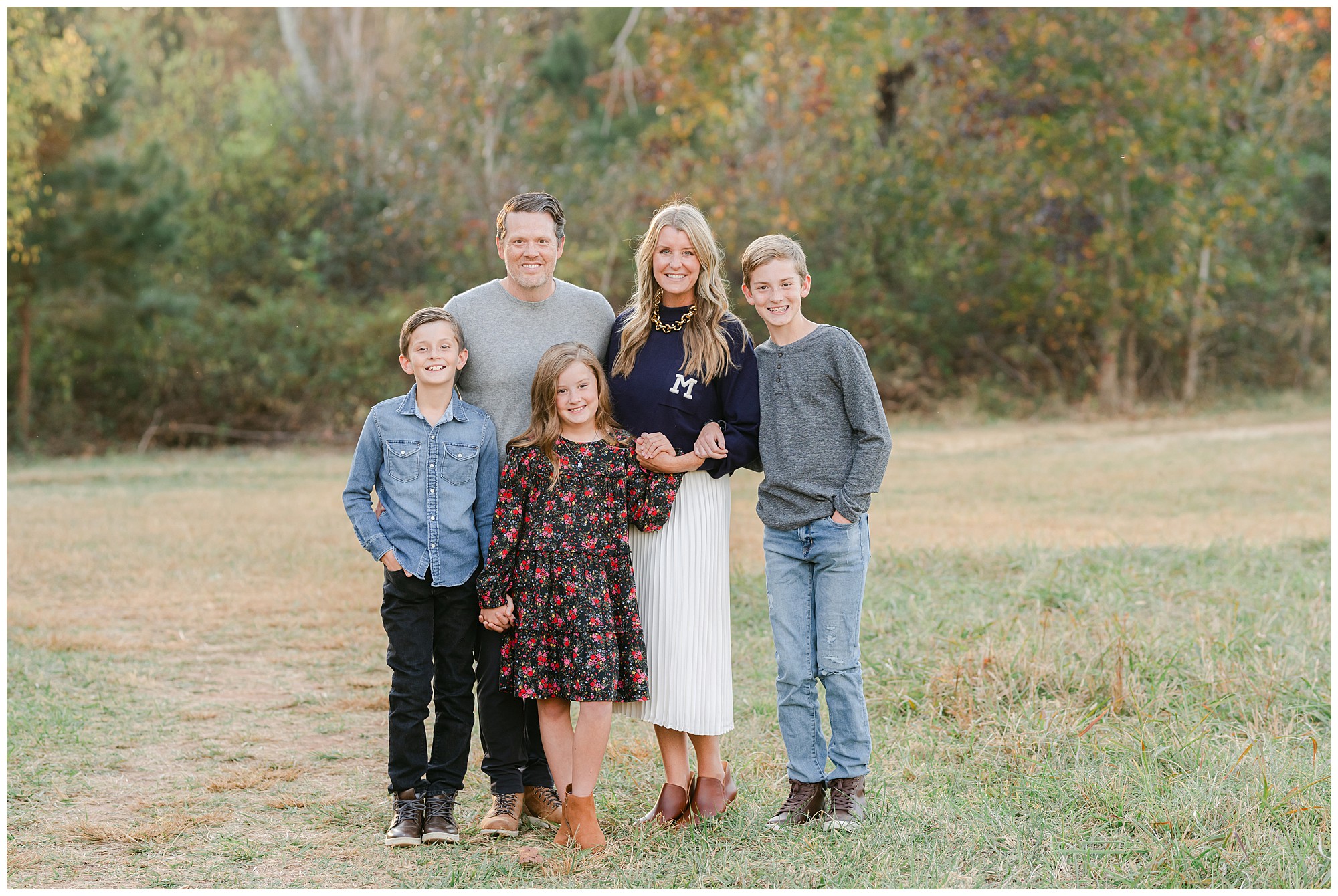 Parents standing with their two sons and daughter in a green field during fall for a portrait by a Marietta family photographer.