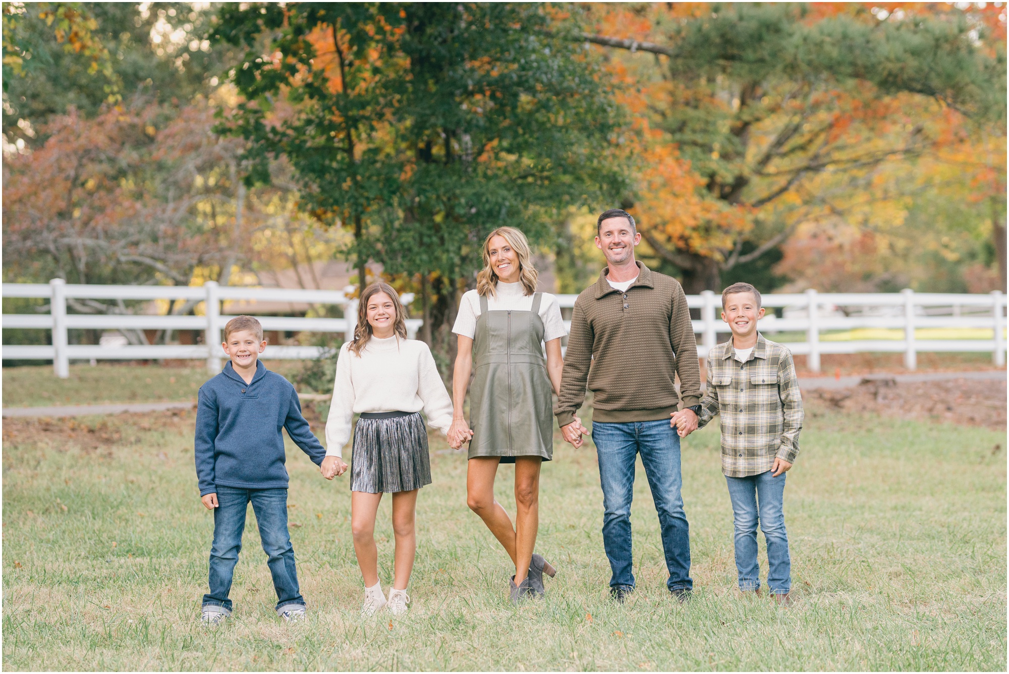 Parents stand in a field holding hands with their two sons and daughter for portraits with Atlanta fall family photographer Lindsey Powell.