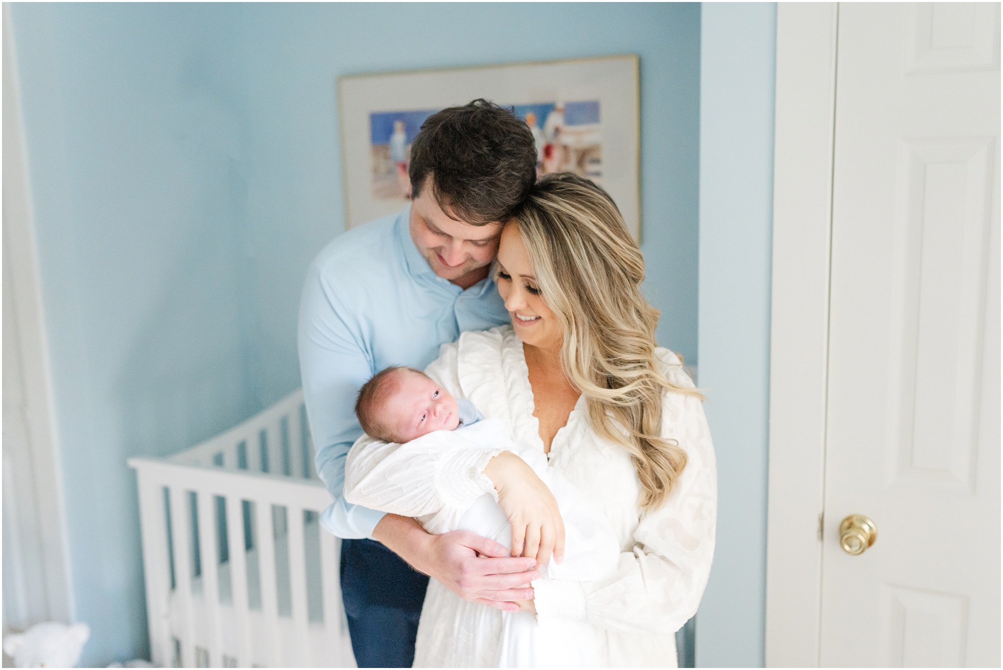 A mother holds her newborn baby boy while his father stands behind her gazing down at his son during Atlanta newborn photos at home.