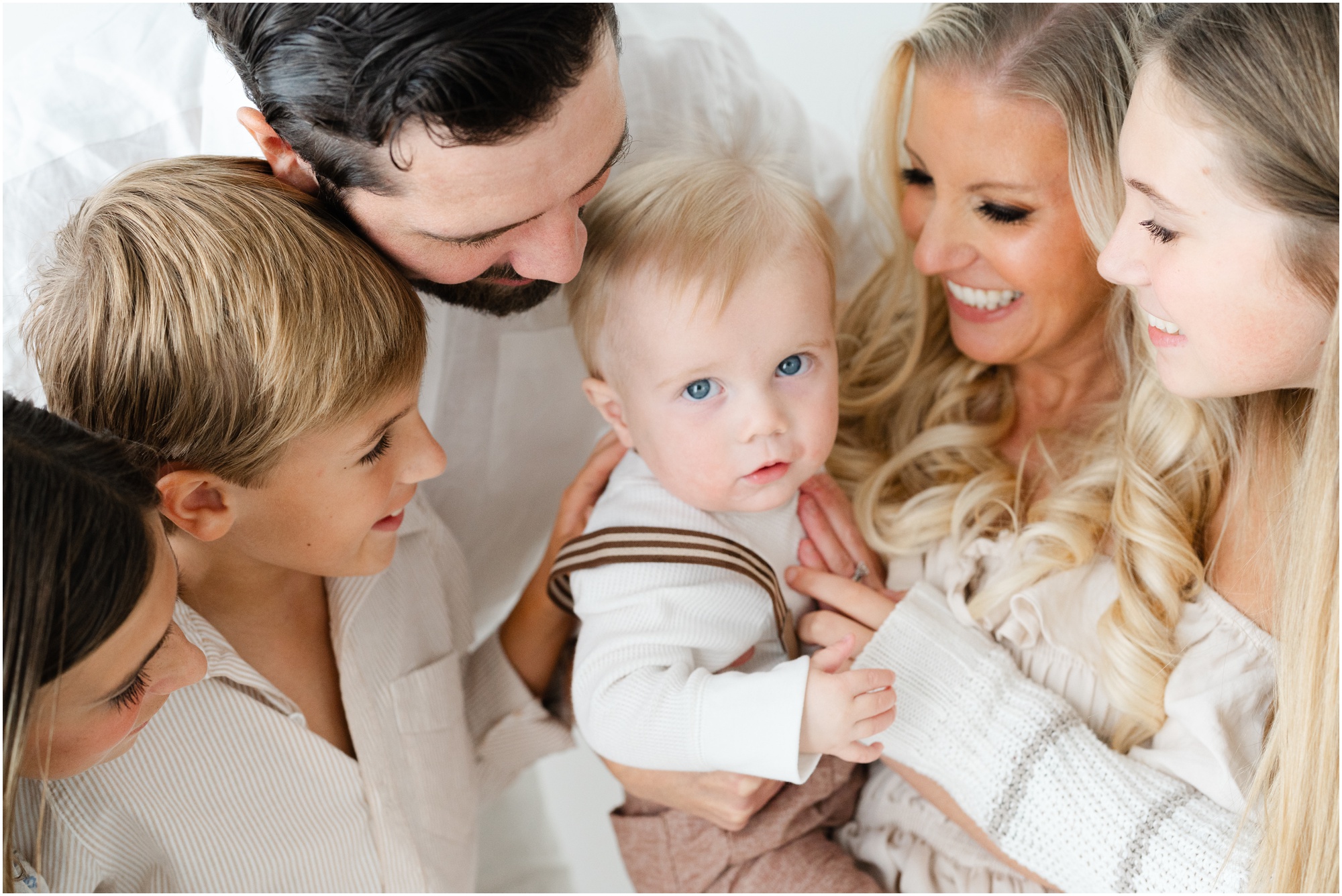 A baby boy gazes up at the camera with his family surrounding him and smiling down at him during his Atlanta First Birthday Portraits.