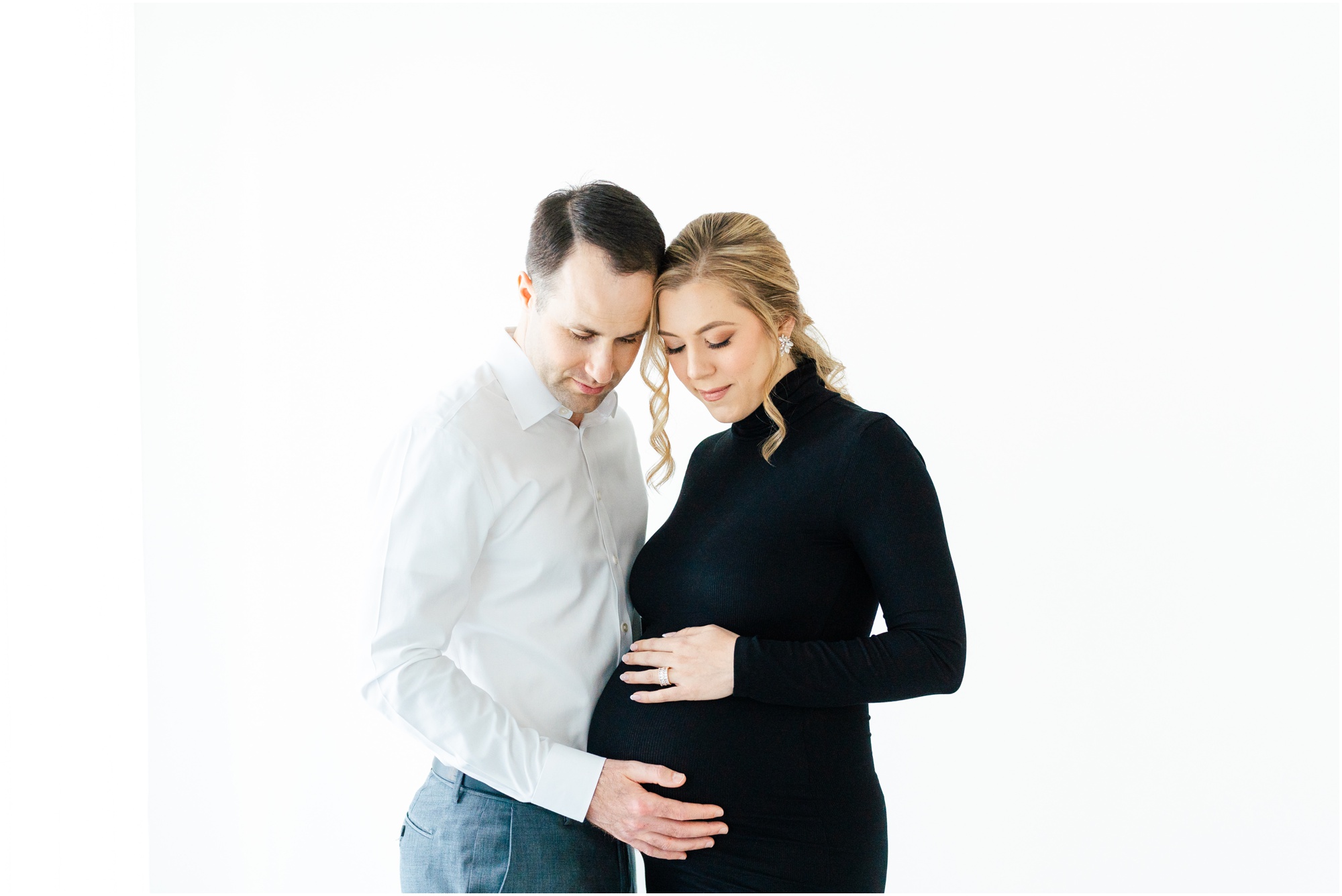 Atlanta maternity photos of a women in a black turtleneck fitted dress cradling her belly with her husband.