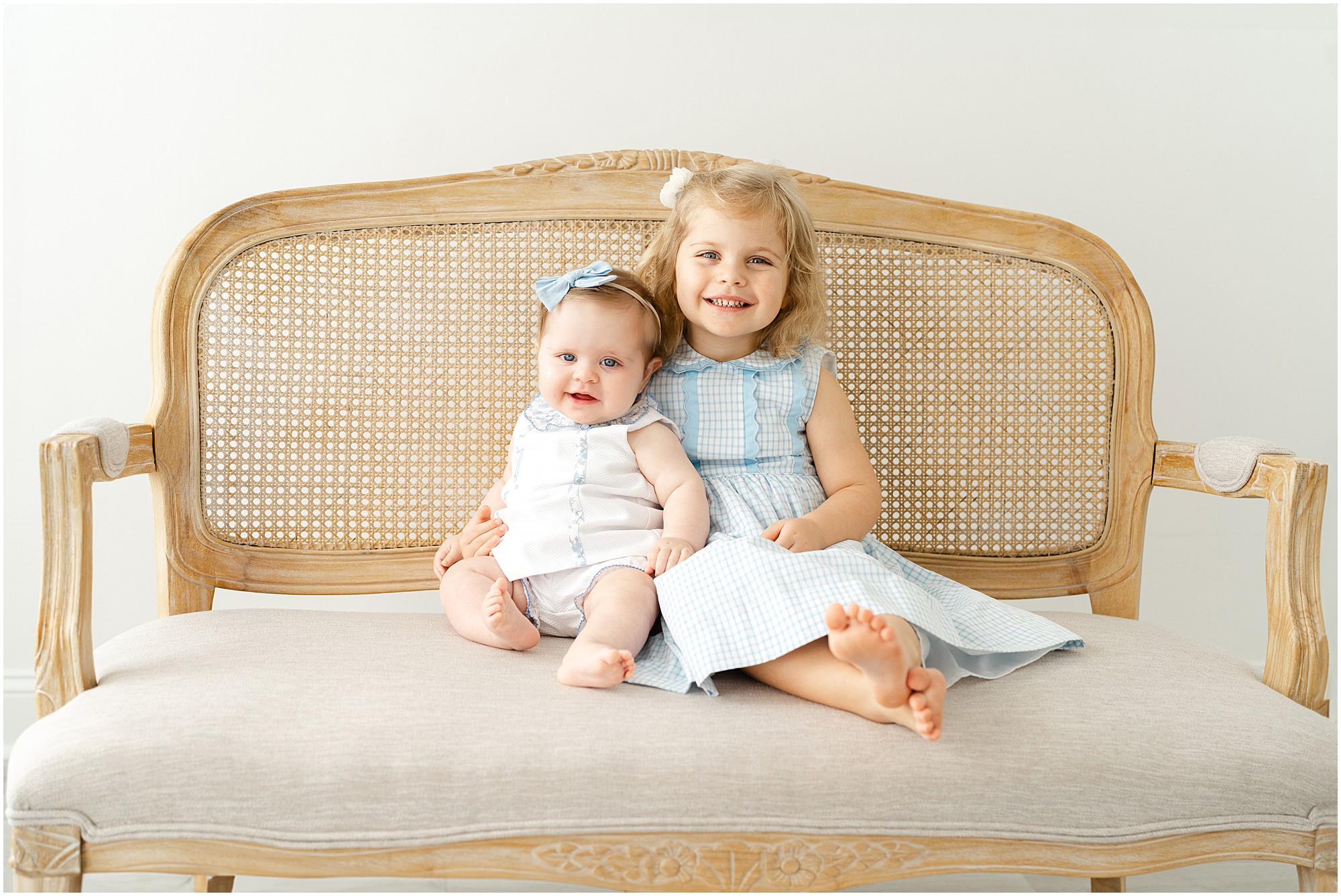 Portrait of a baby and her toddler sister on a bench in a Marietta GA photography studio.