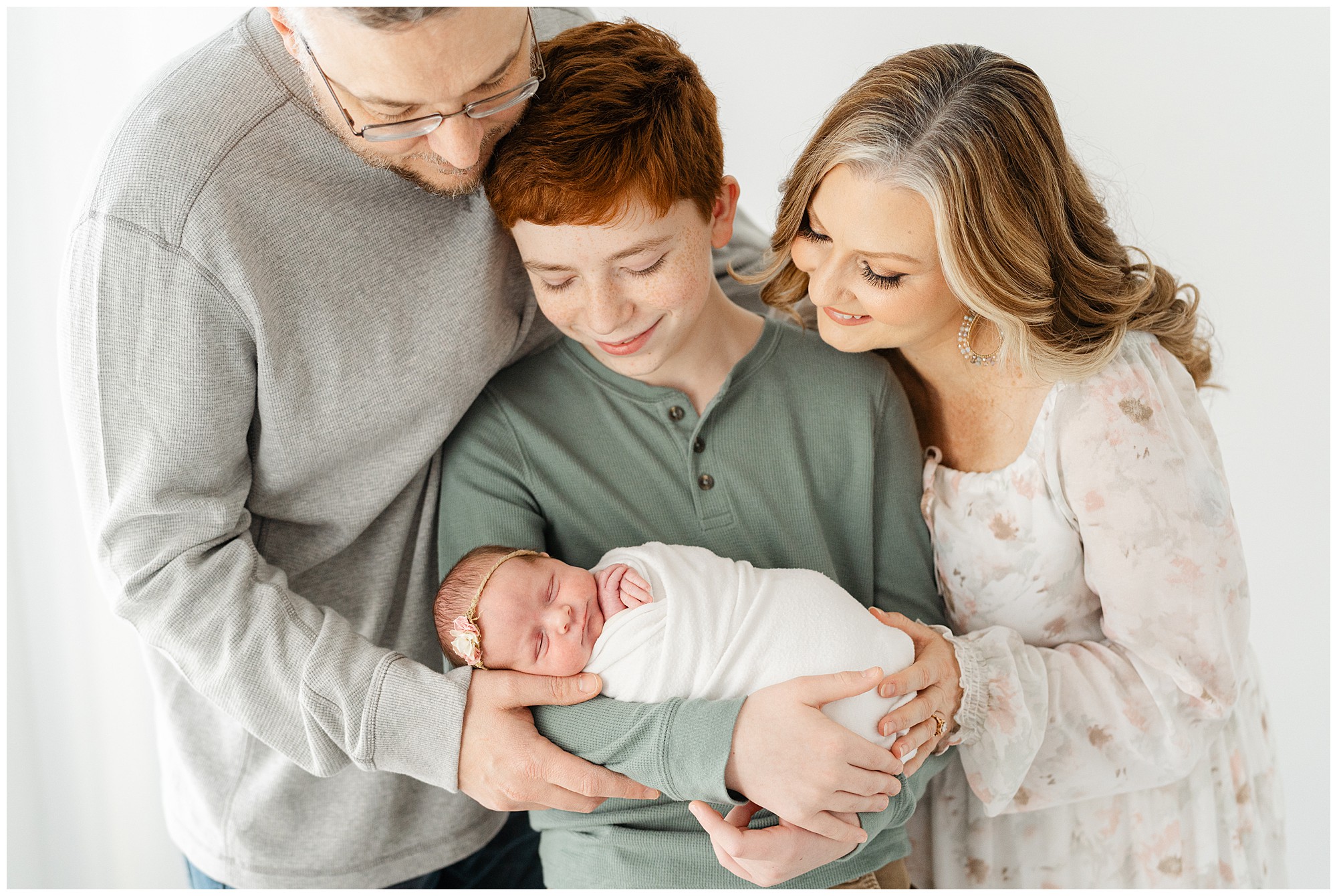Portait of a young boy holding his newborn sister with his mom and dad hugging him and looking down at the baby in an Atlanta studio newborn photography session.
