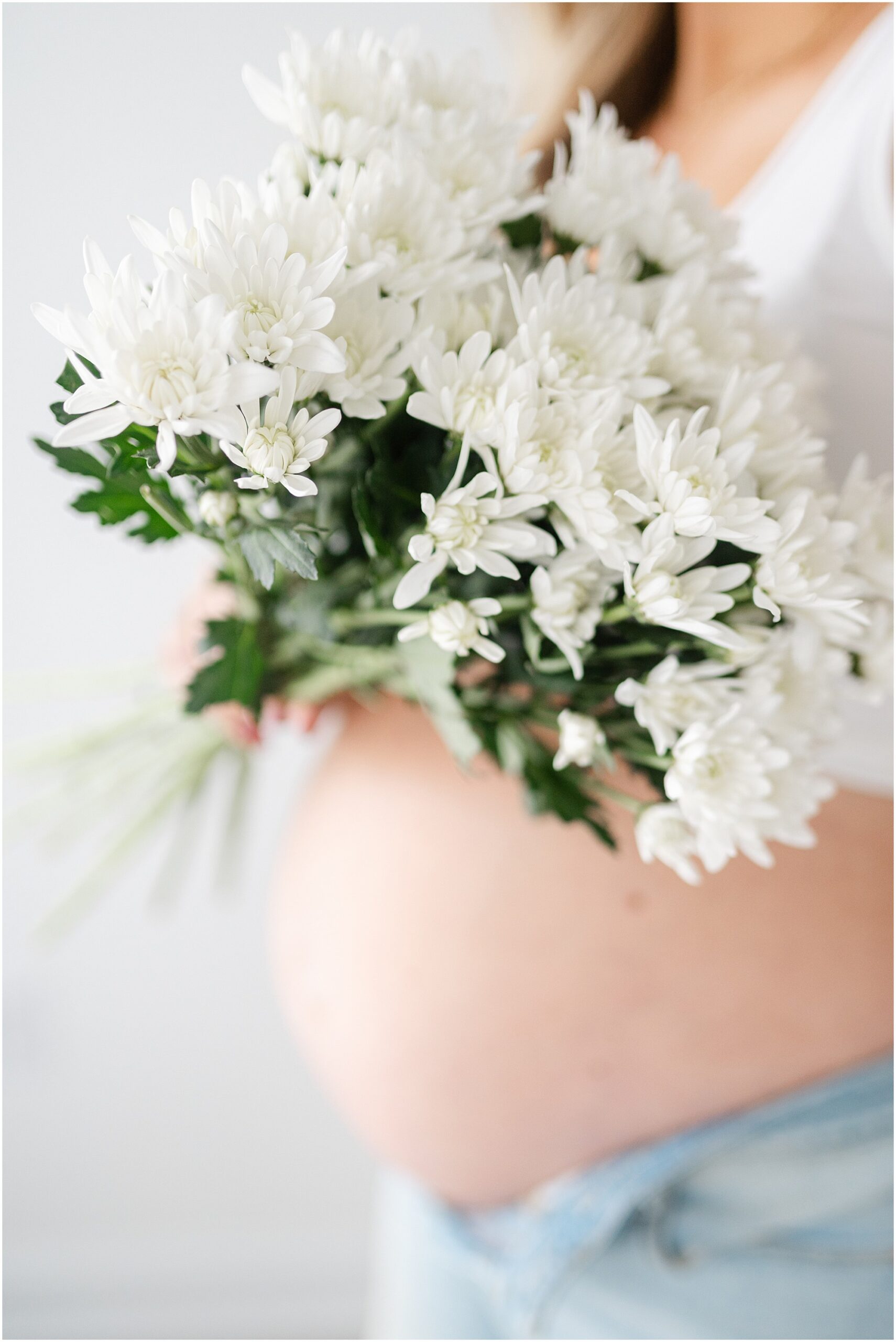 Portrait of white flowers by a mother's bare baby bump during a Marietta maternity session.