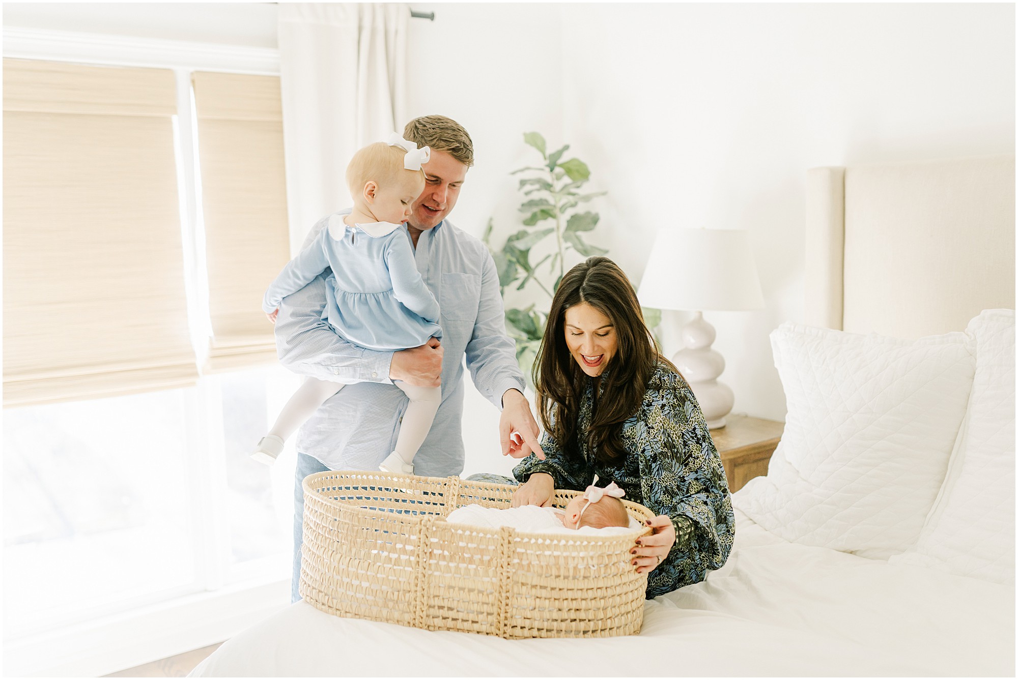 Parents and a toddle look down with smiles at a newborn in a Moses basket during an in home Marietta newborn photo session.